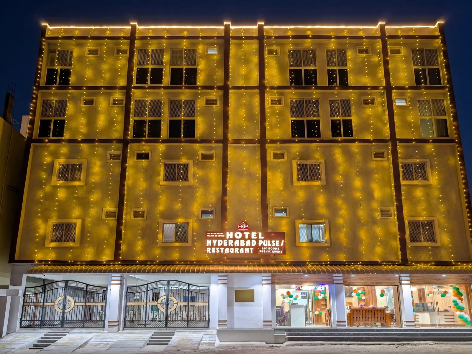 The Hotel Hyderabad Pulse building at night, its facade lit with string lights