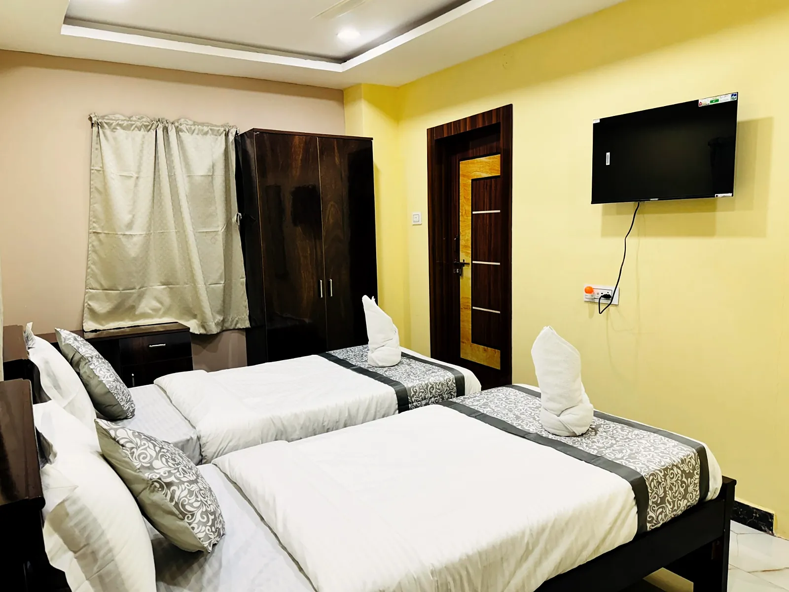 Twin room with a wall-mounted television, a wardrobe and a curtained window at Hotel Hyderabad Pulse